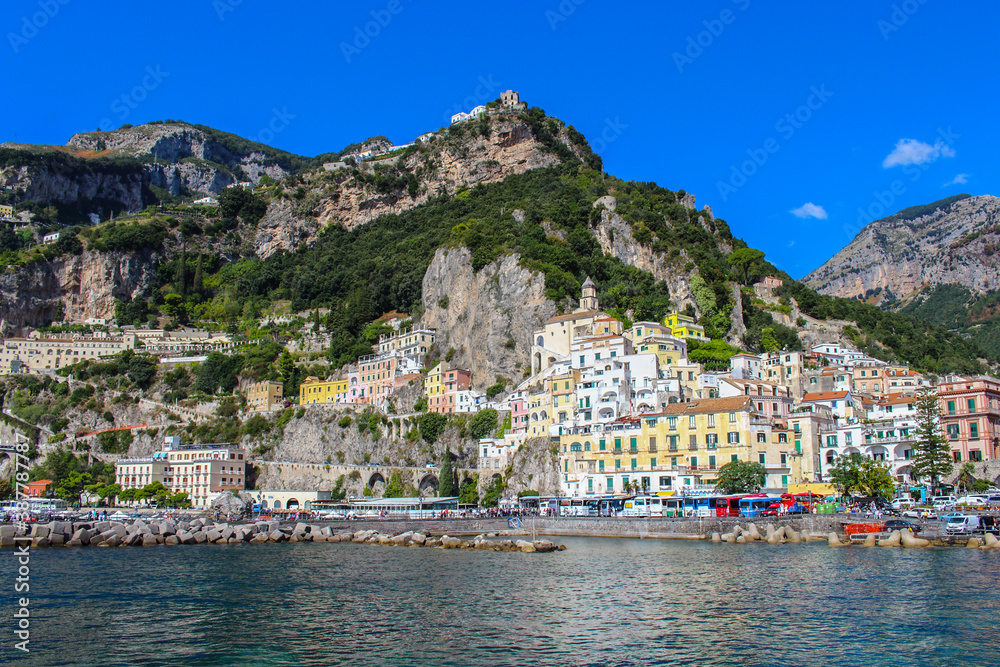 View of the city of Amalfi from the jetty with parked buses, the sea and the colorful houses on the slopes of the Amalfi coast in the province of Salerno, Campania, Italy.