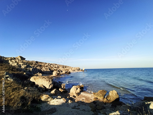 Sea waves crash against rocks on a wild stone beach. Calm sea water. White clouds in the blue sky. sea rest. large stones. foam.