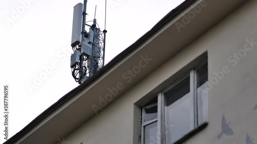 Antennas for cellular transmitters on roof of residential building. Facade of house with windows. Mobile phone tower next to housing. Radio emission. High-frequency interference. Microwave signal