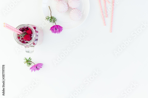 Berries smoothie with straws, marshmallow and anemones flowers on white background. Flat lay