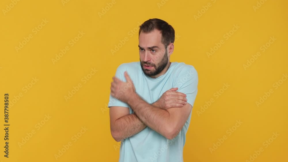 Bearded fun young man 20s in basic casual blue t-shirt isolated on yellow background studio. People lifestyle concept. Look camera rubs his hands froze season feel bad not healthy first signs of cold