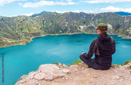 Young male backpacker enjoying the landscape of the Quilotoa volcanic lake on the highest peak at 3930m altitude along the Quilotoa Loop hike, Quito, Ecuador.