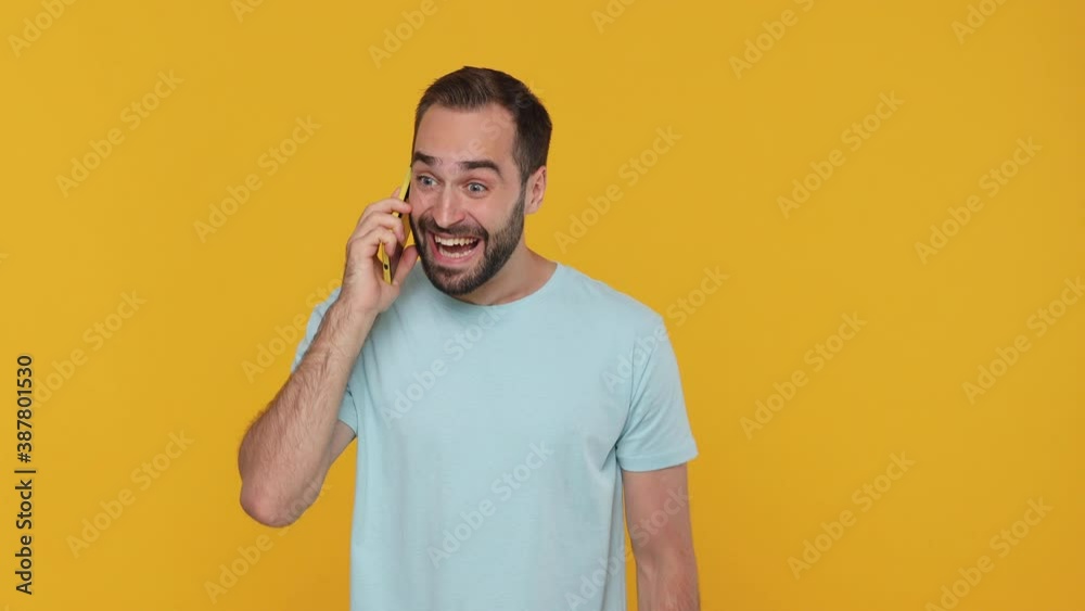 Bearded happy excited young guy in basic casual blue t-shirt using speaking talking on mobile cell phone just found out great big win news isolated on yellow background studio People lifestyle concept Bearded happy excited young guy in basic casual blue t-shirt using speaking talking on mobile cell phone just found out great big win news isolated on yellow background studio People lifestyle concept