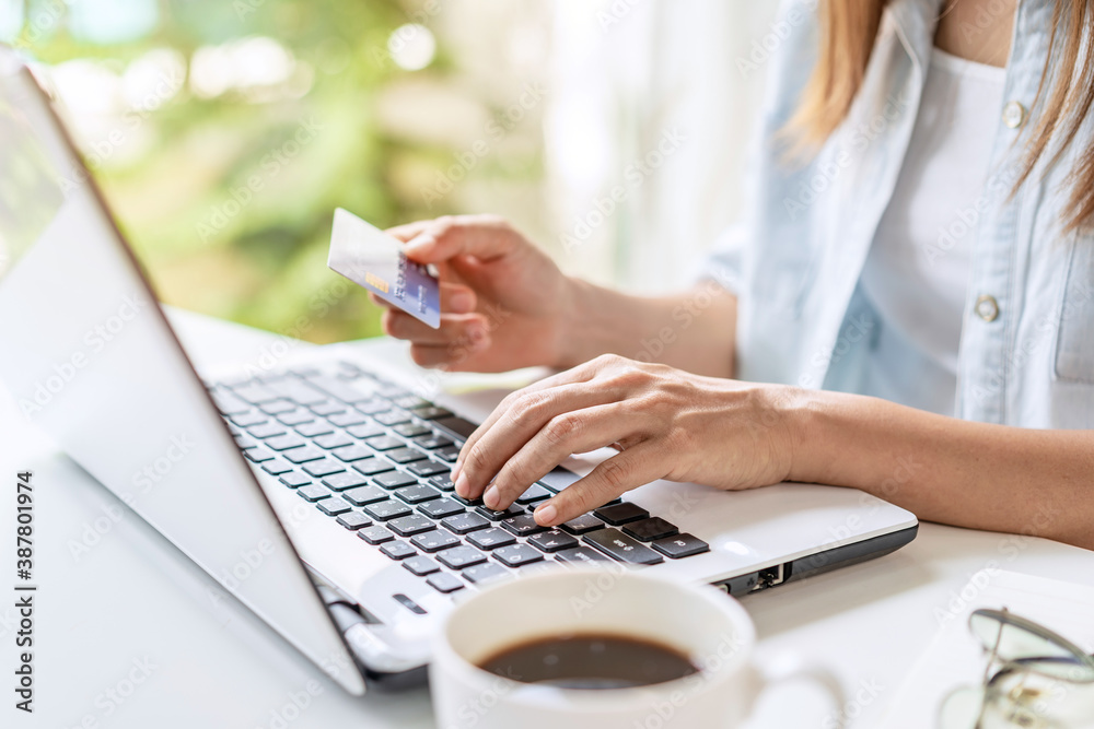 Fototapeta premium Young woman holding a credit card and using computer for making online payment shopping