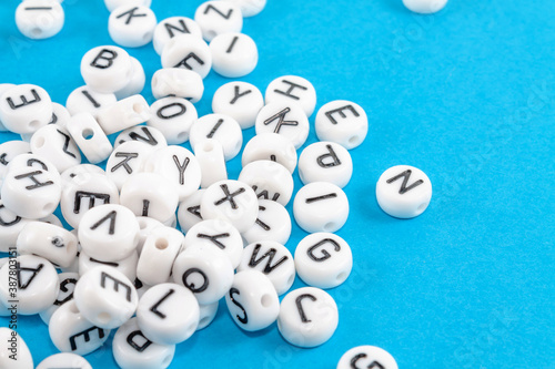 A lot of scattered white small round blocks with black English letters to produce words. Close-up on a blue background.