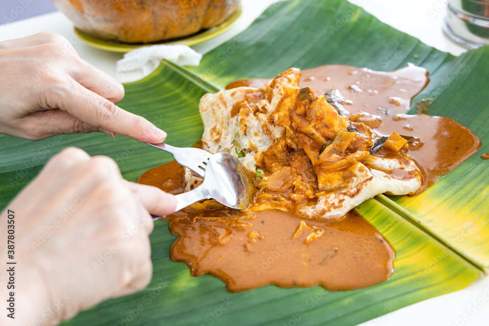 Person eating roti canai or paratha served with curry served on banana leaf