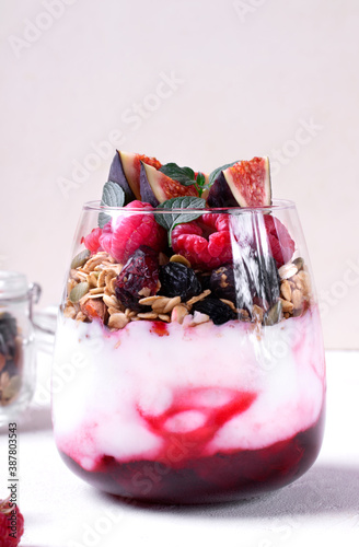 Layered trifle dessert in the glass on the white table. Cherry jam  natural yogurt  granola and raspberry topped with mint. Breakfast idea