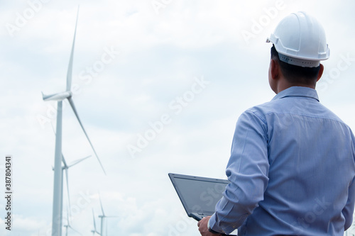 Engineers windmills are working on laptop with the wind turbine in background