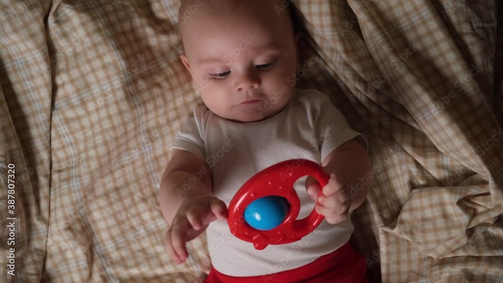 Infant baby boy playing with rattle toy lying in bed. Infant baby boy playing with rattle toy lying in bed.