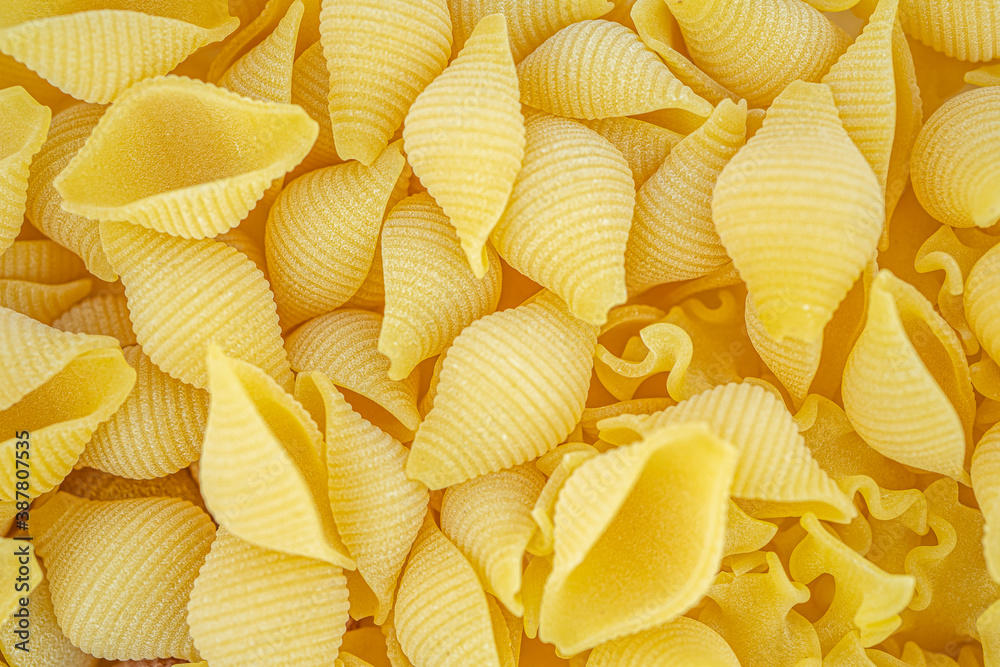 Italian pasta in the shaped of seashells with natural yellow color. Textured background. Macro close up, selective focus. Italian pasta in the shaped of seashells with natural yellow color. Textured background. Macro close up, selective focus.