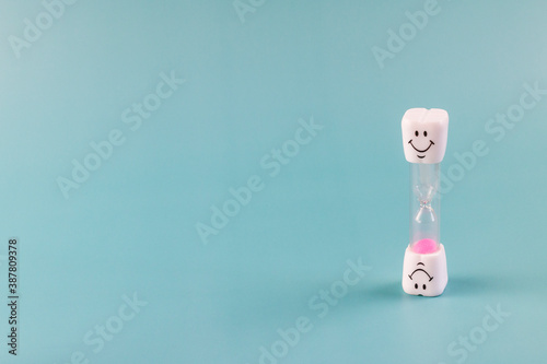 Concept of recommended time for brush teeth. Hourglass. Brushing teeth for 3 minutes. Sand clock with smiley face. Blue background