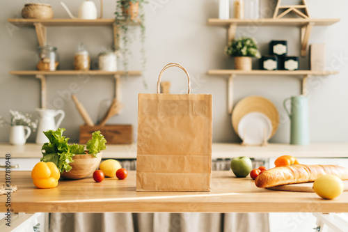 Eco shopping paper bag with fresh vegetables and baguette on the table in modern kitchen. Food delivery or market shopping concept.