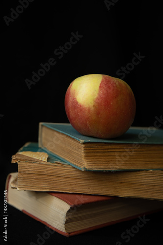 red apple on a stack of old books on a black background