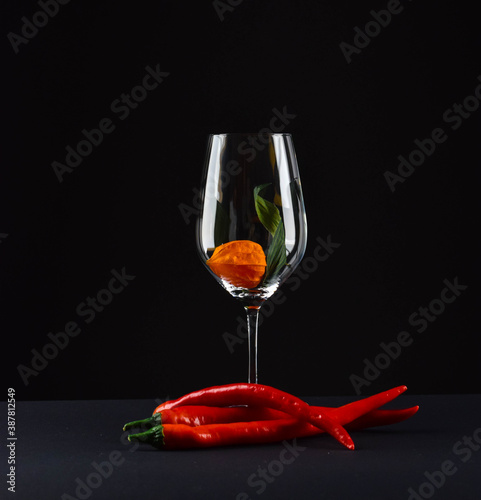 beautiful glass on a black background, a glass of red wine, hot pepper, still life