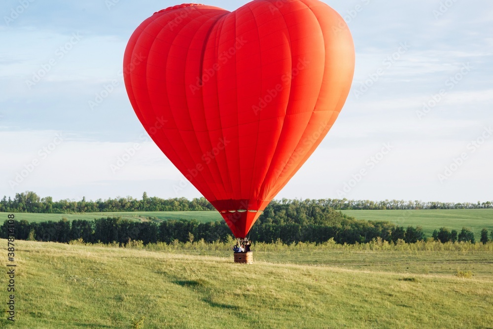 Fototapeta premium Hot air balloon in shape of heart is landing on the green field