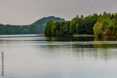 Lake with its calm waters and reflection surrounded by abundant trees and green vegetation  cloudy day with a gray sky in Maasmechelen Belgium.  Inspiration and meditation in a magical place