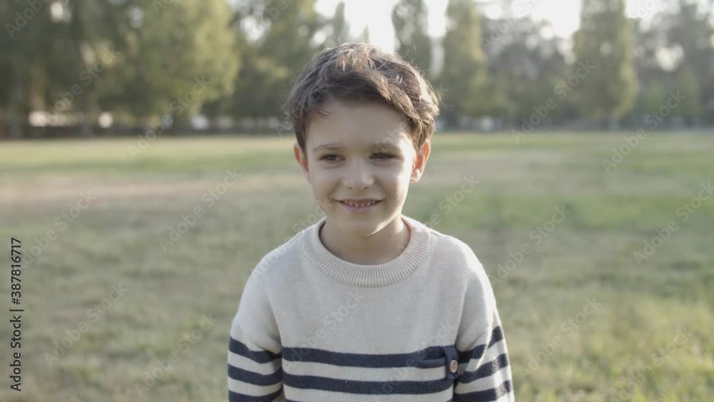 Portrait of lovely Caucasian boy smiling and jumping on camera. Happy cute kid standing on lawn, posing on nature and looking at camera. Front view. Expression, emotion and appearance concept Portrait of lovely Caucasian boy smiling and jumping on camera. Happy cute kid standing on lawn, posing on nature and looking at camera. Front view. Expression, emotion and appearance concept