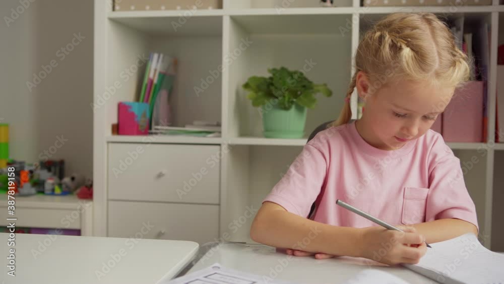 Tracking medium shot of elementary school girl writing in notepad, thinking and using laptop while learning sitting at desk at home Tracking medium shot of elementary school girl writing in notepad, thinking and using laptop while learning sitting at desk at home