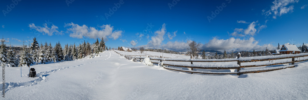 Winter remote alpine village outskirts, snow drifts on mountain fir forest edge. Tourist backpack on a freshly trodden hiking trail path. Winter remote alpine village outskirts, snow drifts on mountain fir forest edge. Tourist backpack on a freshly trodden hiking trail path.