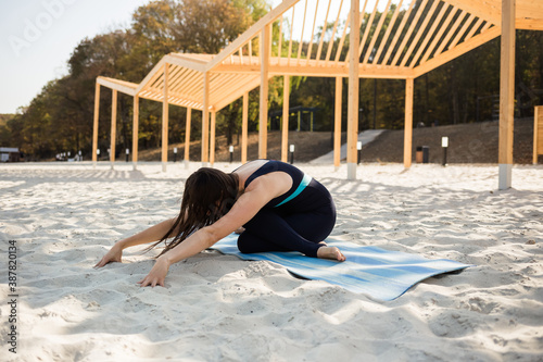 a female yogi lies in the Virasana pose on a blue Mat on a sandy beach. Side view photo