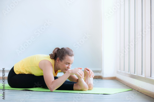 Young caucasian women Yoga exercising seated forward bend and touch at foot position pose wearing sportswear on green pad indoors, It is an exercise that makes the body strong. Feel relaxed and calm.