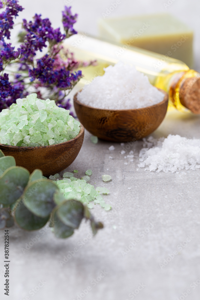 Sea salt in bowl, aroma oil in bottles, Wellness and flowers on grey textured background and flowers on vintage wooden background. Selective focus.