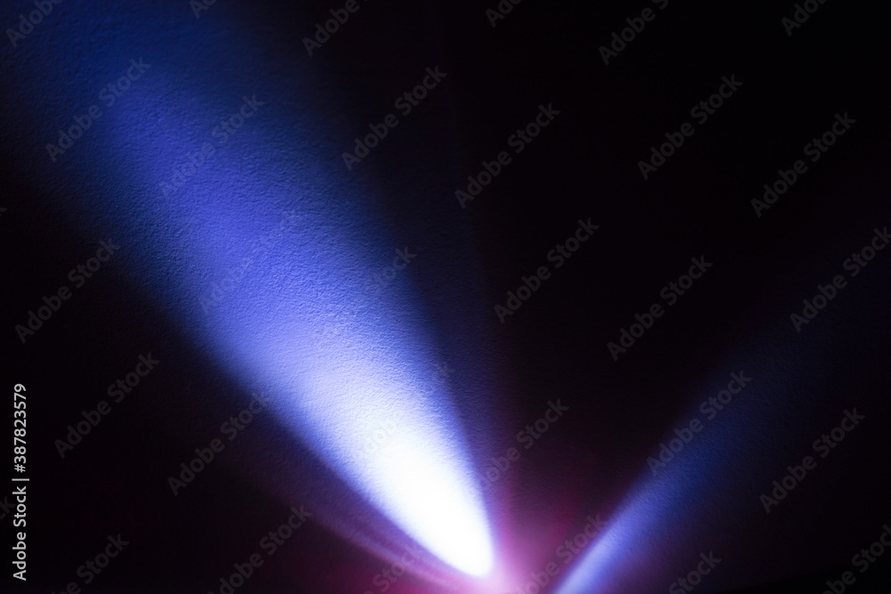 Cool blue light from an LED flashlight on a white wall. A ray of light on the surface. Cool blue light from an LED flashlight on a white wall. A ray of light on the surface.