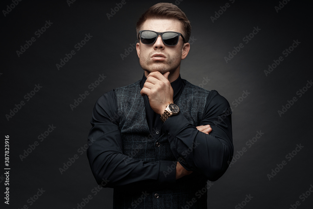 Portrait of beautyful guy on dark background. High fashion model posing in studio. Attractive man in classic suit and sunglasses. - obrazy, fototapety, plakaty 