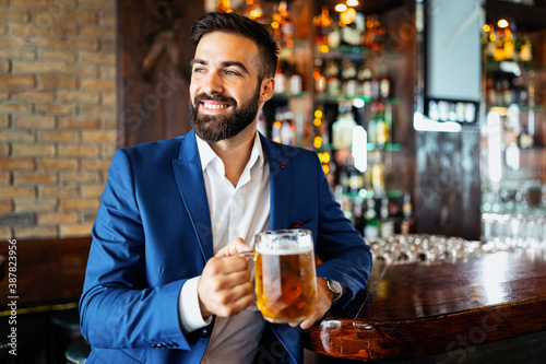 Happy businessman raising glass of beer after work in a pub