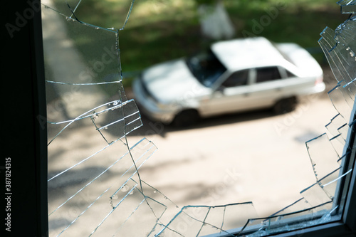 View of a car standing on the street, through a broken window in an apartment building. Selective focus. Defocused.