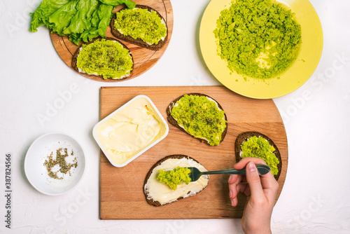 Female chef prepares an avocado sandwich. Table with a plate of mashed avocado, spices, bread and a pack of cream cheese