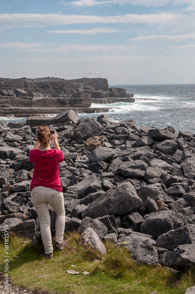 Young woman with a red shirt on a cliff to take a picture with her phone to Ireland coastline