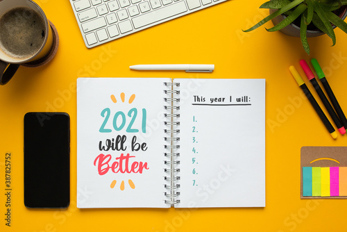 Stock photo of 2021 new year notebook with list of goals, motivational phrase and objects on yellow background 