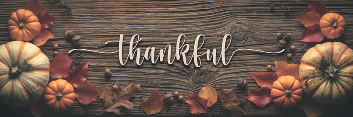 
"Thankful" Message On Rustic Harvest Table Background Decorated With Pumpkins Acorns And Leaves 