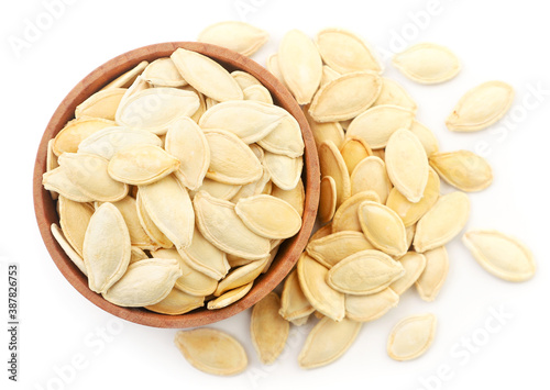 Pumpkin seeds in a wooden plate and scattered close-up on a white. Top view.