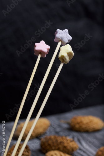 Marshmallows on a stick. Against the background of pine boards in black. Nearby are spruce cones.