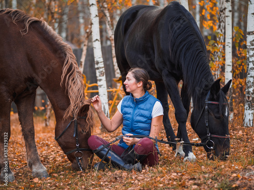 Girl and two horses are walking in the autumn park