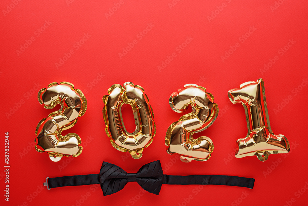gold foil balloons numbers 2021 with black bow tie on red background, new year's composition, festive dinner concept, top view, copy space gold foil balloons numbers 2021 with black bow tie on red background, new year's composition, festive dinner concept, top view, copy space