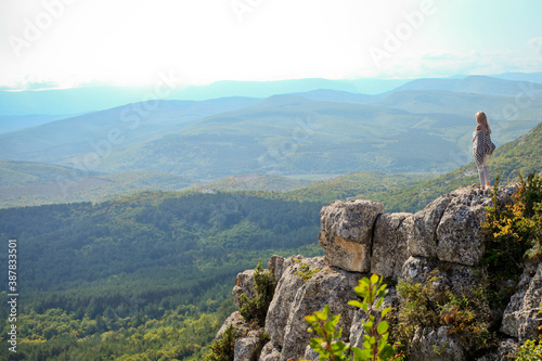 A young traveling woman stands on the edge of a mountain cliff and watching a beautiful view of the forest, mountains and clouds on vacation. The woman travels alone. © smile35