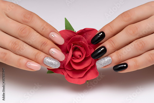 Black  beige  silver  shiny manicure with crystals on short oval nails close-up on a white background with a red rose in hands.