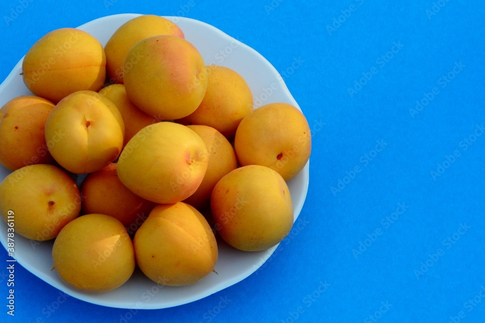 Fresh apricots on a plate on blue bright background close up
