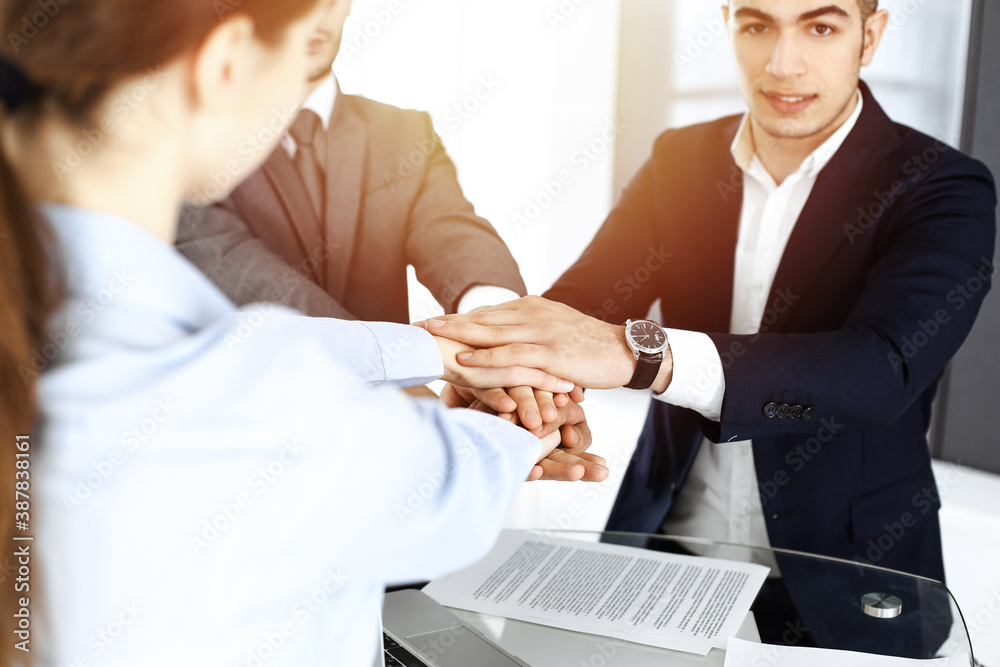 Business people group showing teamwork, joining hands and giving five to each other in sunny office