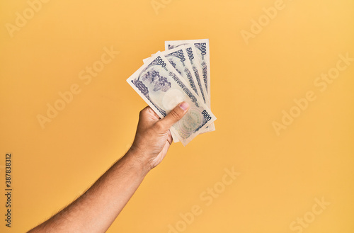 Bilde på lerret Hand of hispanic man holding japanese yen banknotes over isolated yellow background