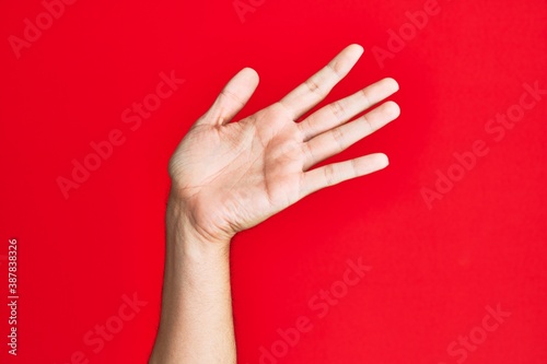 Arm of caucasian white young man over red isolated background presenting with open palm  reaching for support and help  assistance gesture