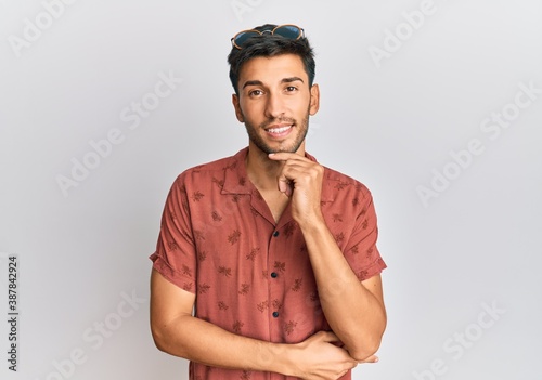 Young handsome man wearing casual summer clothes looking confident at the camera smiling with crossed arms and hand raised on chin. thinking positive. © Krakenimages.com