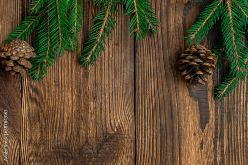 Fir, spruce branches, pine cones on brown wooden background with copy space