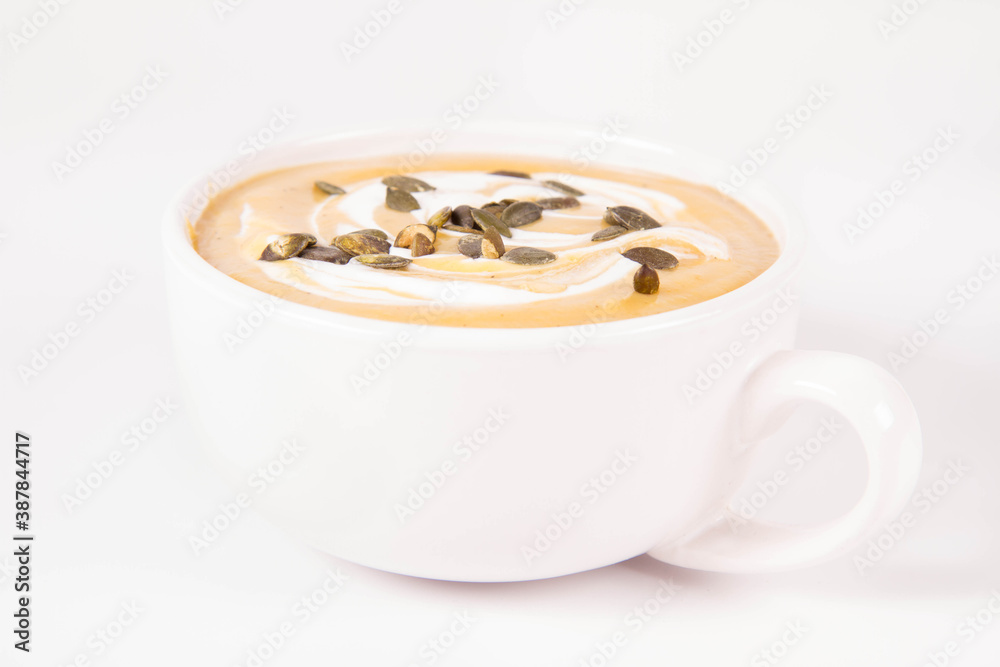 Pumpkin soup decorated with cream and pumpkin seeds in a bowl on a white background Pumpkin soup decorated with cream and pumpkin seeds in a bowl on a white background