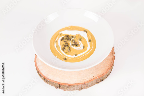 Pumpkin soup decorated with cream and pumpkin seeds on a plate on a piece of wood