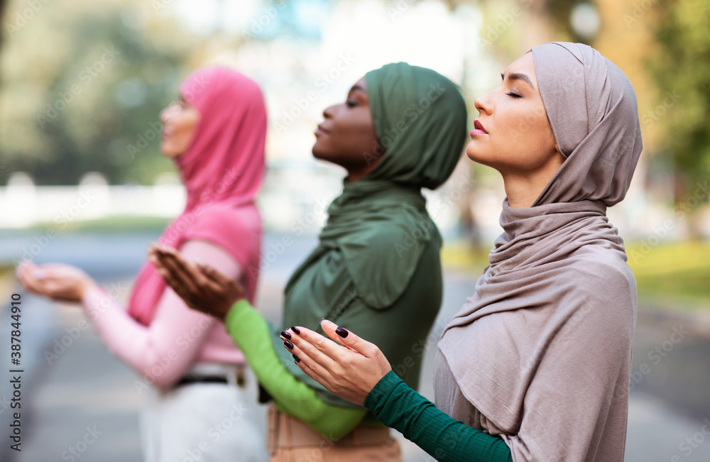 Three Muslim Women Praying Together Standing Outdoors Wearing Traditional Hijab - obrazy, fototapety, plakaty 