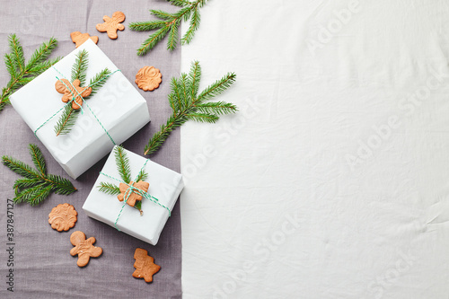 Christmas gifts wrapped in white paper and decorated with spruce sprigs and gingerbread cookies